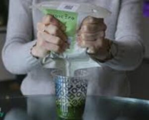 Mãos espremendo saquinho de suco em um copo.